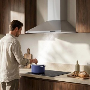 Silberne CIARRA Wandhaube 60 cm über Kochfeld, Mann kocht. Dunstabzugshaube mit LED-Beleuchtung in moderner Küche.