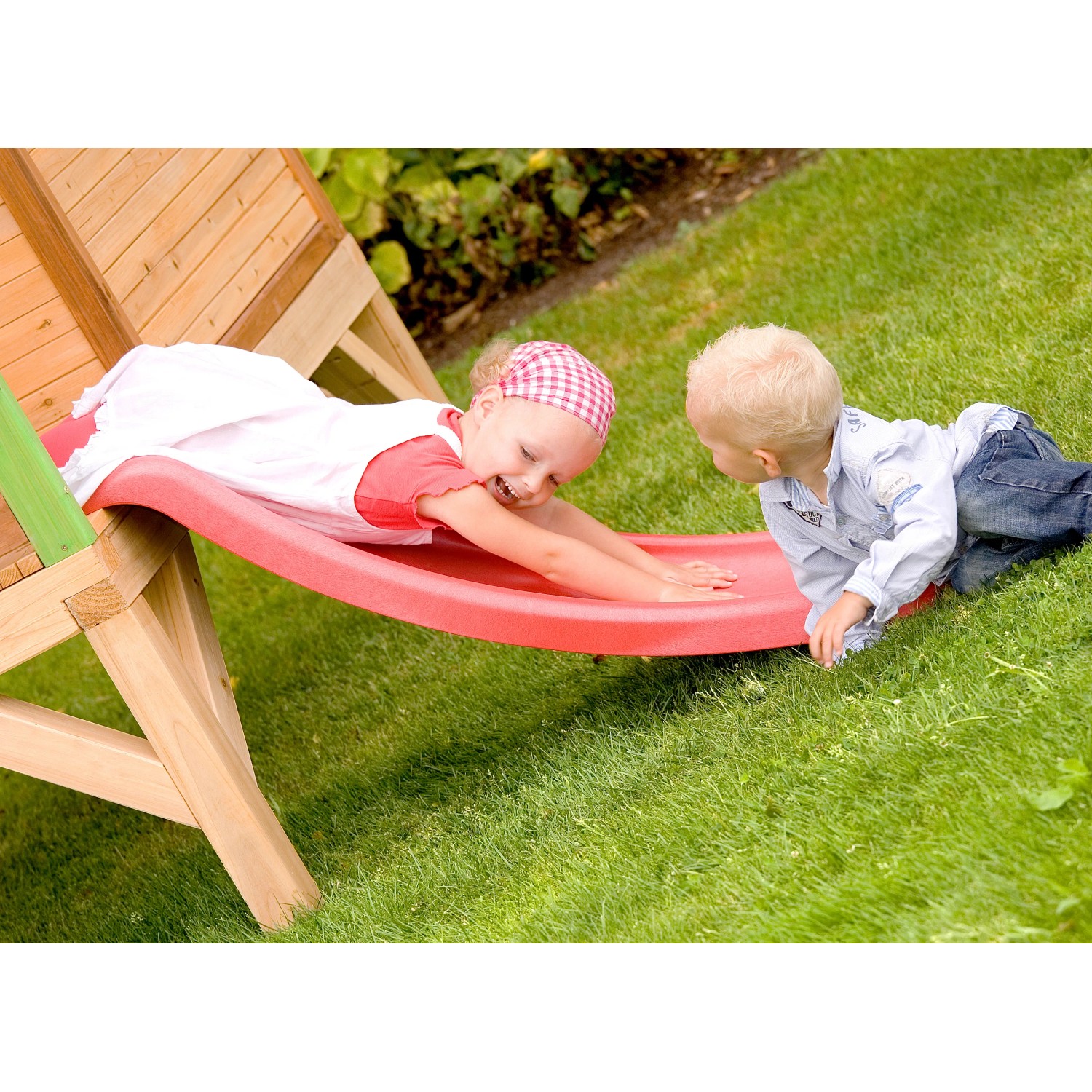 Kinder spielen auf der roten Rutsche des Axi Tom Spielhauses im Garten.