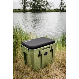 Petromax Kühlbox kx50 in Oliv, 50 Liter Fassungsvermögen, mit schwarzem Sitzkissen vor einem See.