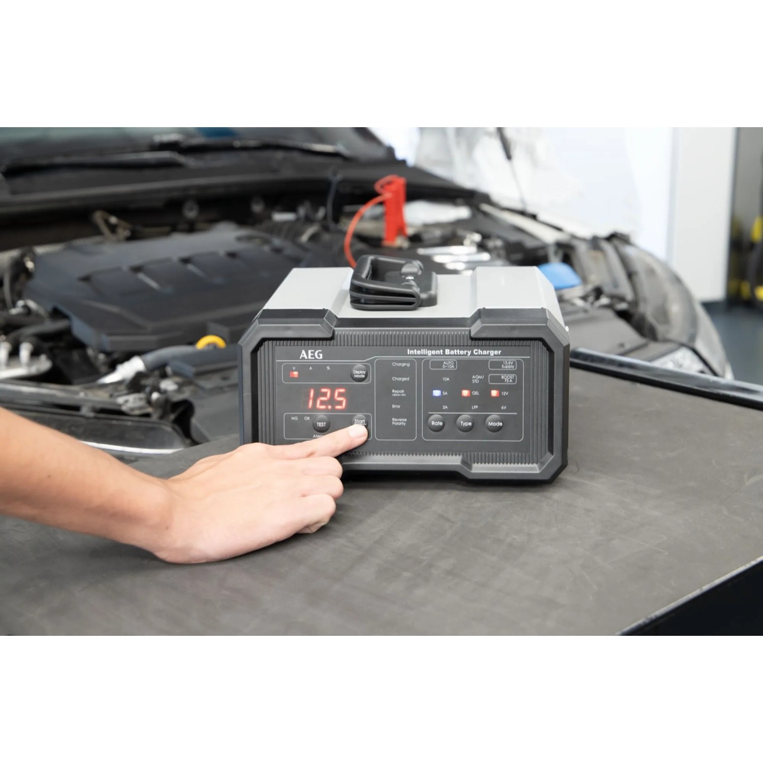 AEG Batterieladegerät CW10 in Anwendung vor einem Auto, digitales Display zeigt 12.5