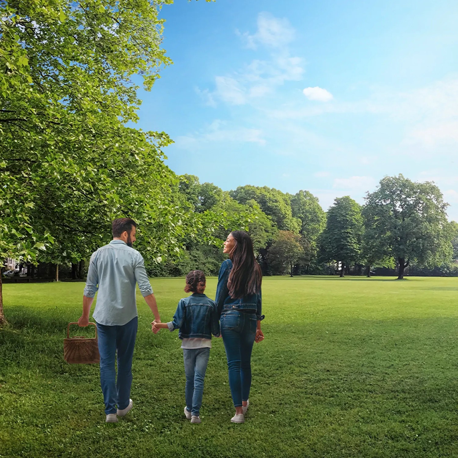 Familie mit Picknickkorb geht durch einen Park mit grünen Bäumen und blauem Himmel.