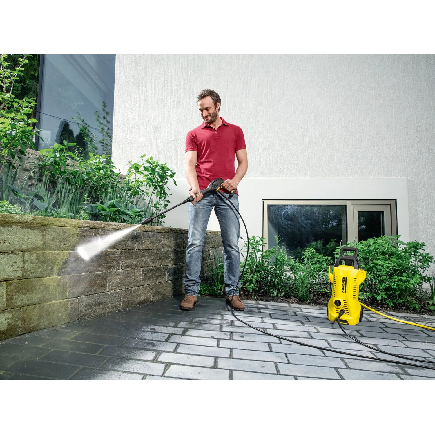 Mann reinigt Mauer mit gelbem Kärcher Hochdruckreiniger K 2 Power Control.