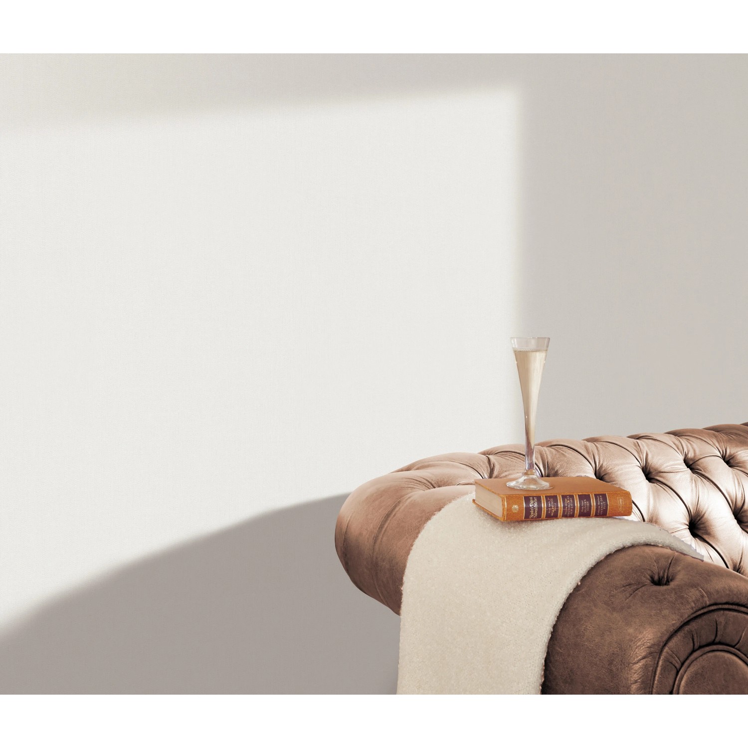 Weiße Erismann Vliestapete Spotlight InStyle an Wand über braunem Sofa mit Buch und Glas.