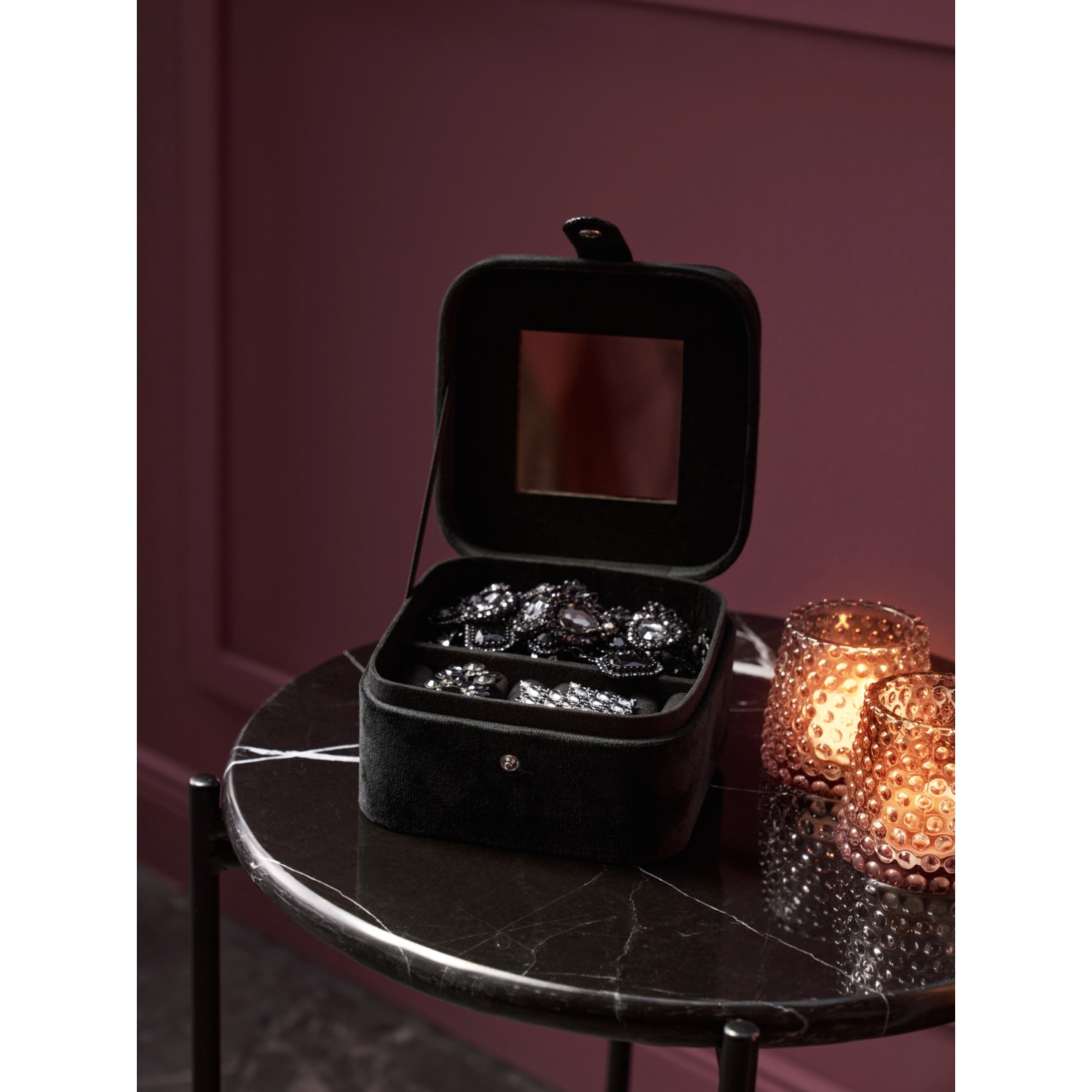 Geöffnete, schwarze Schmuckbox Midnight Mystery mit Spiegel und Schmuck auf einem Tisch.