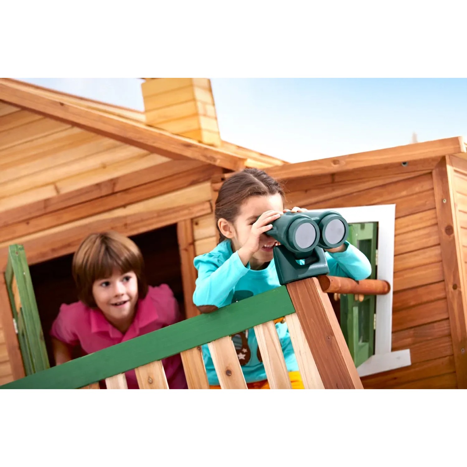 Kinder spielen im Axi Spielhaus Max mit Leiter, Rutsche und Sandkasten. Das Holzhaus ist braun und grün.