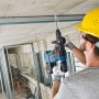 Arbeiter bohrt mit blauem Bosch Professional Akku-Bohrhammer GBH 18V-26 in Betondecke auf Baustelle.