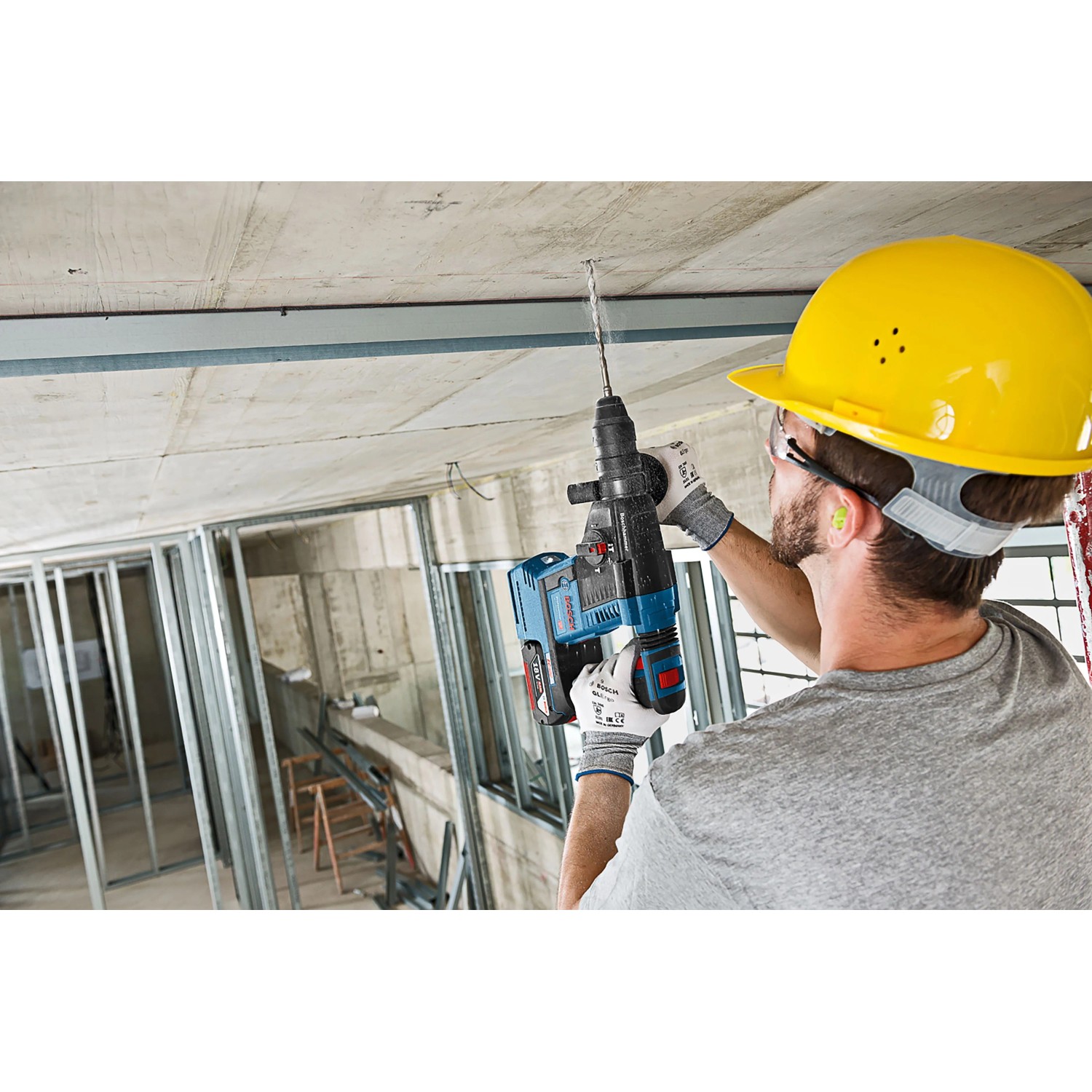 Arbeiter bohrt mit blauem Bosch Professional Akku-Bohrhammer GBH 18V-26 in Betondecke auf Baustelle.