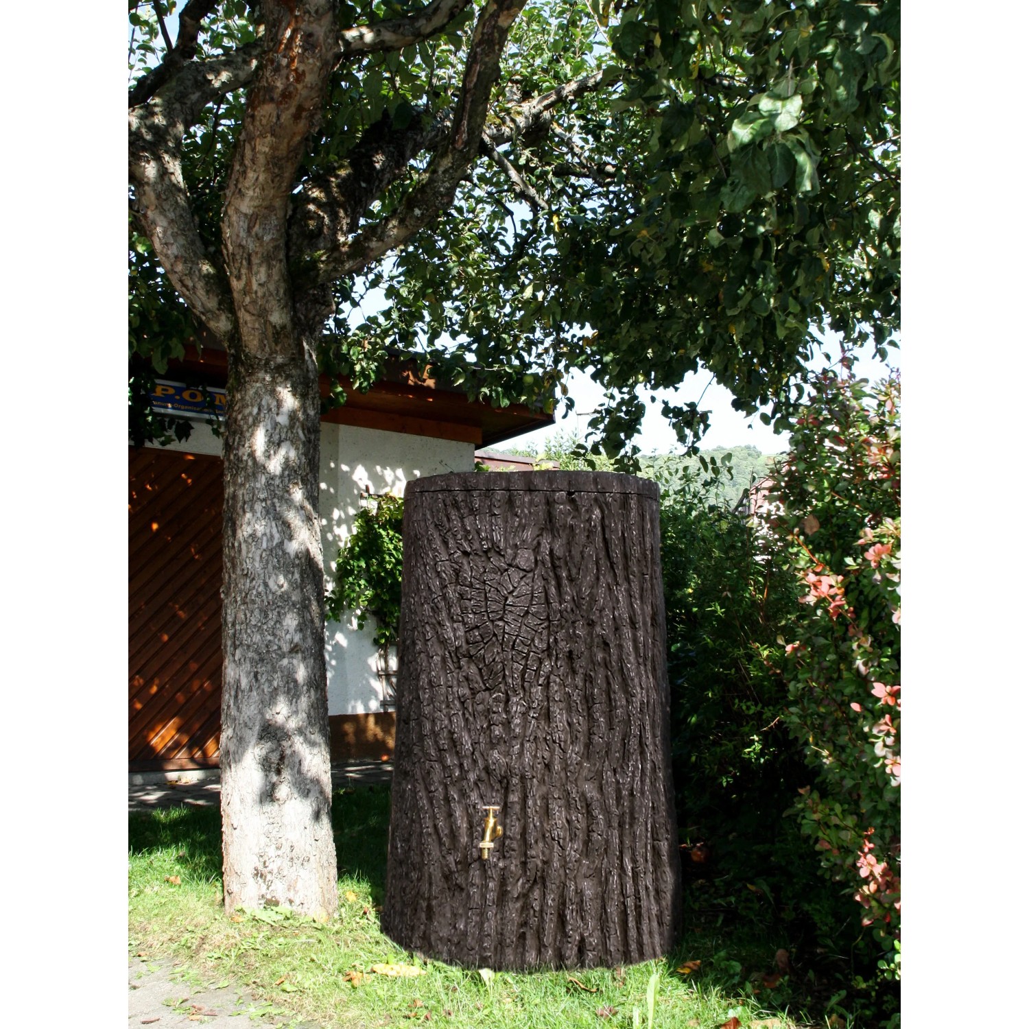 Arves Regentonne Evergreen, 475 l, dunkelbraun, Baumstammoptik mit Zapfhahn im Garten.