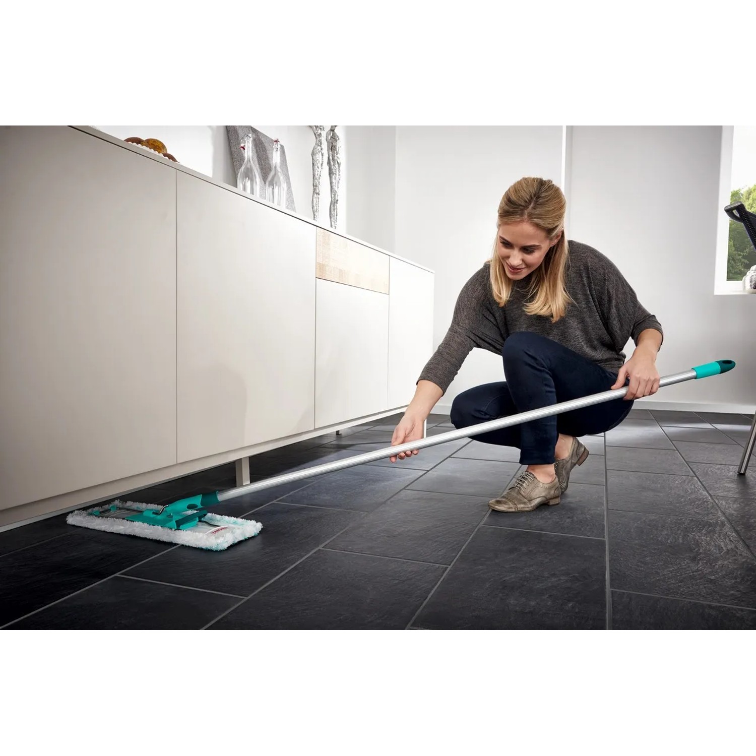 Frau wischt Fliesenboden mit Leifheit Bodenwischer Profi XL Micro Duo unter einem Schrank.