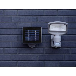 Lutec Solar LED-Strahler Sunshine mit Solarpanel an dunkler Backsteinwand.