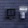 Lutec Solar LED-Strahler Sunshine mit Solarpanel an dunkler Backsteinwand.