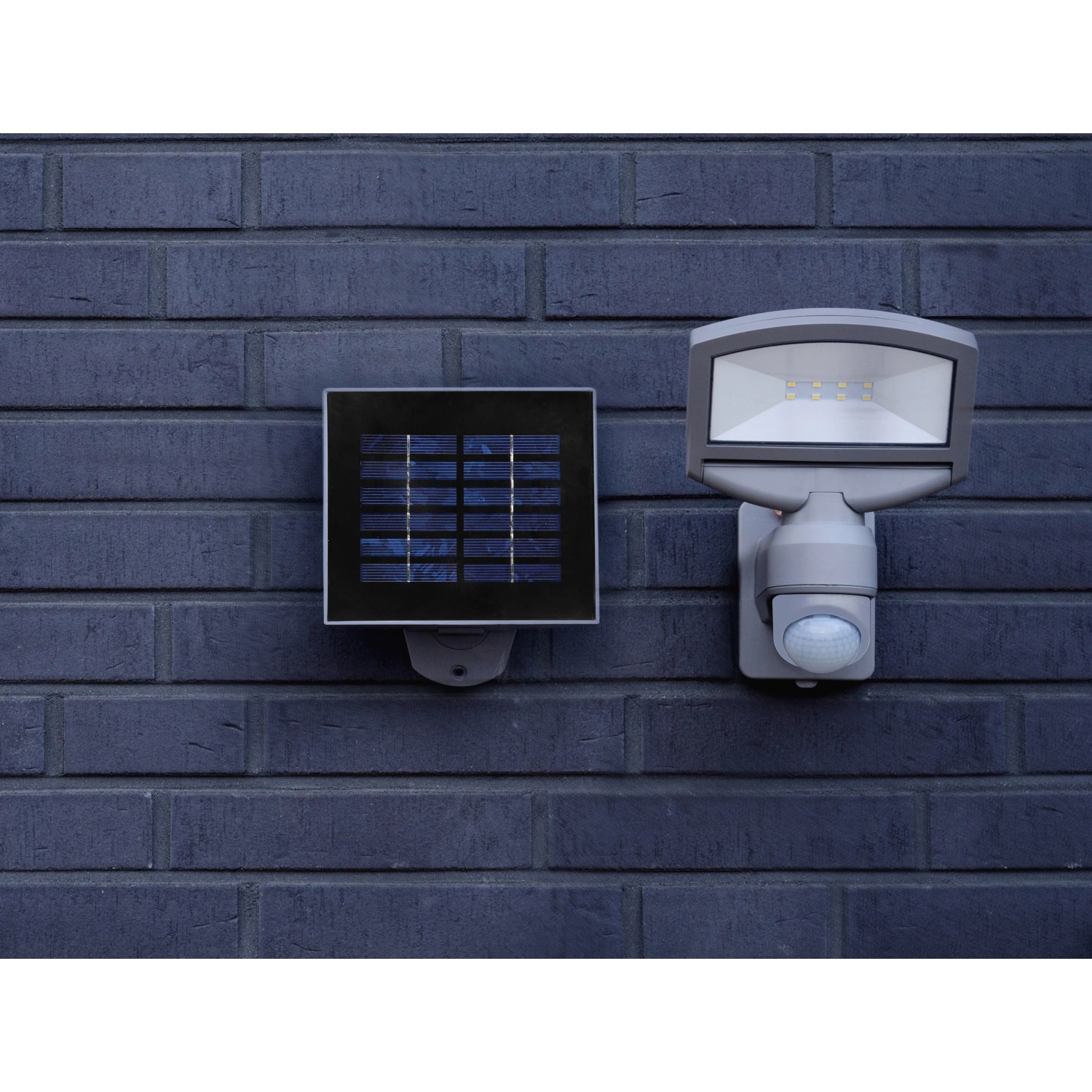 Lutec Solar LED-Strahler Sunshine mit Solarpanel an dunkler Backsteinwand.