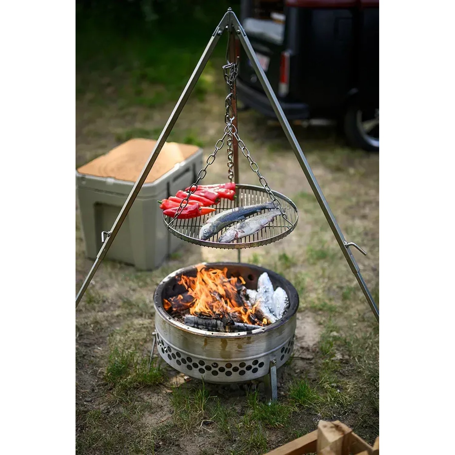 Petromax Hänge-Rost am Dreibein über Feuerstelle mit Fisch und Paprika. Grillutensil für Lagerfeuer.