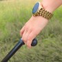 Hand hält einen schwarzen Gehstock mit goldener Smartwatch am Handgelenk vor grünem Hintergrund.
