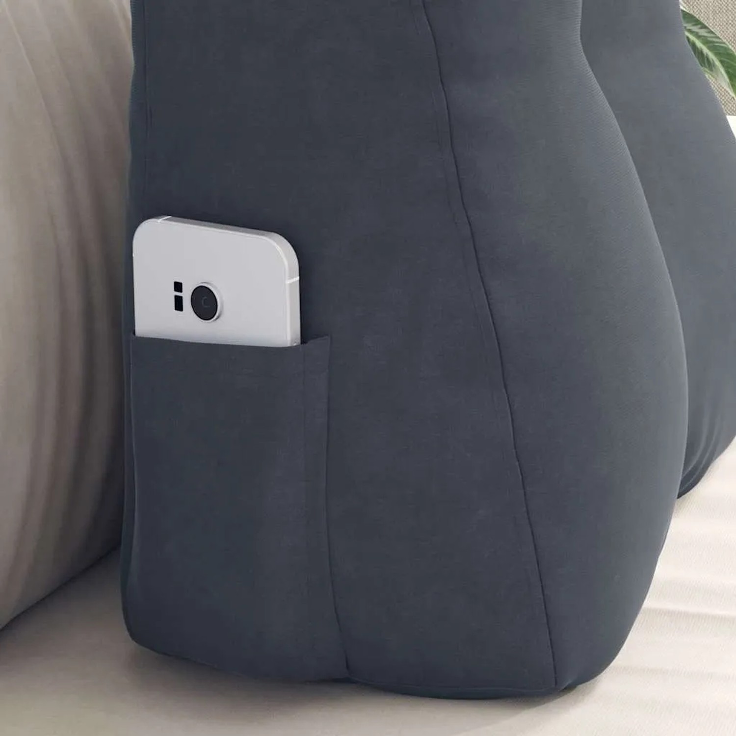Dunkelgraues Samt-Rückenkissen mit Seitentasche, in der ein Smartphone steckt. Weich und praktisch.