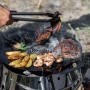 Petromax Atago Grill-Set mit Grillgut auf runder Grillplatte im Freien.