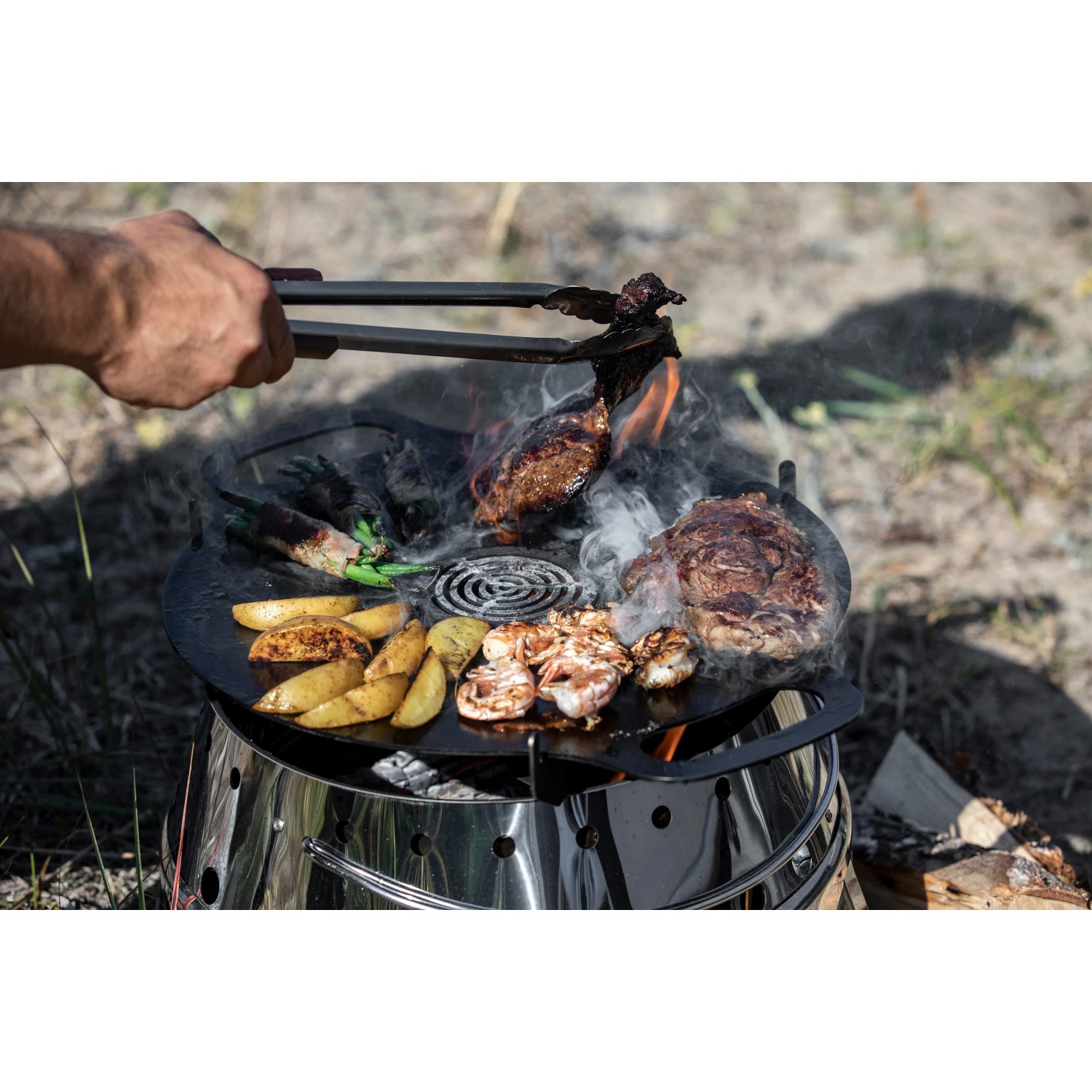 Petromax Atago Grill-Set mit Grillgut auf runder Grillplatte im Freien.