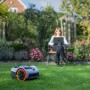 Segway Navimow Mähroboter i105E im Garten, Frau mit Laptop im Hintergrund.