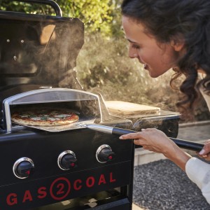 Frau schiebt Pizza mit Char-Broil Pizzaschieber in Grillofen.