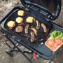 Schwarzer Weber Gasgrill Traveler Compact mit Grillgut und Beilagen auf Seitentisch.