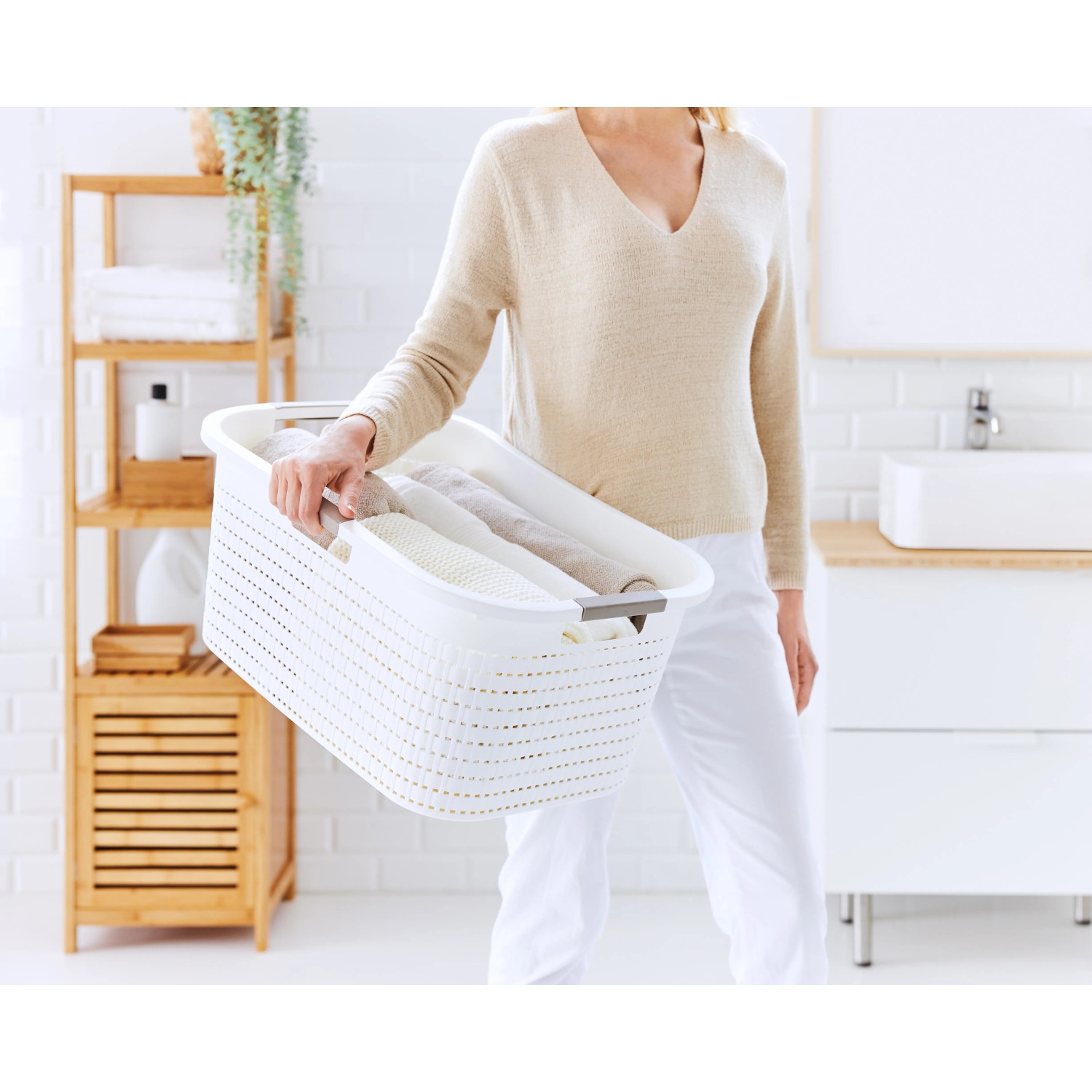 Frau trägt weißen Rotho Wäschekorb Country (40 l) mit Rattanstruktur im Badezimmer.