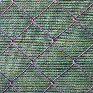 Dunkelgrüne HDPE Zaunblende als Sichtschutz, durch Maschendrahtzaun sichtbar. Wetterfest & UV-stabilisiert für Garten.