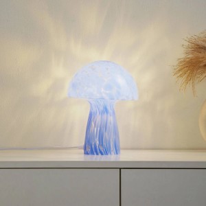 Moderne Lindby Hubi Tischlampe aus blauem Glas in Pilzform, leuchtend auf weißer Kommode. Ideal für Wohnzimmer.
