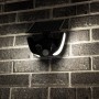 Schwarze LED Solar Wandleuchte Botshabelo mit Sensor an einer Backsteinwand.
