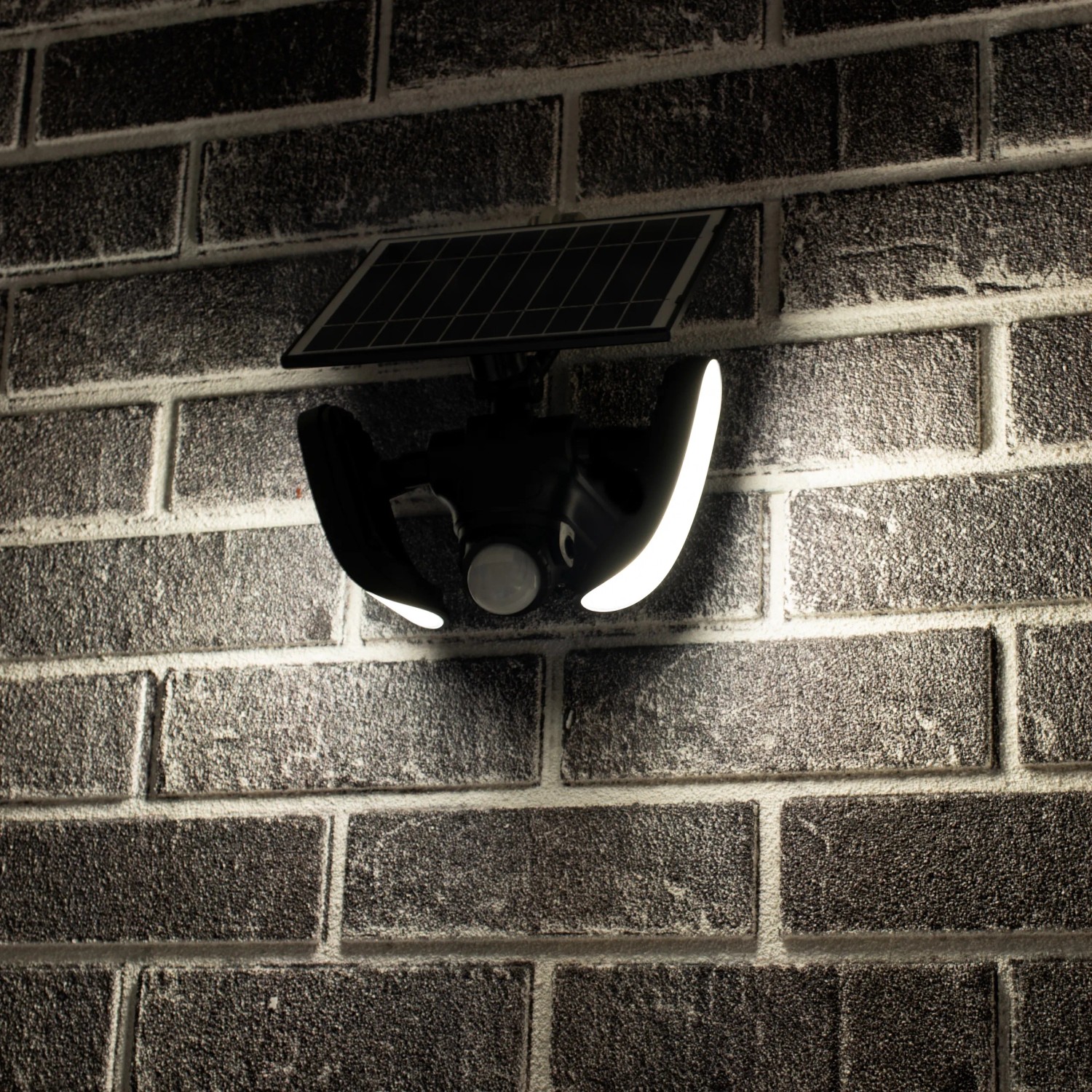 Schwarze LED Solar Wandleuchte Botshabelo mit Sensor an einer Backsteinwand.