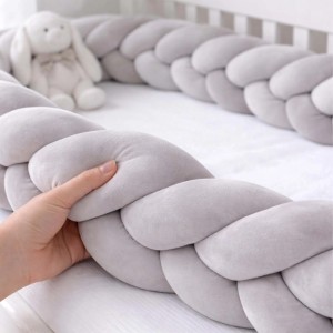 Graue geflochtene Bettschlange aus Polyester im Babybett, eine Hand drückt die weiche Bettumrandung.