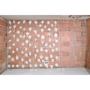 Aufgetragener Knauf Perlfix Ansetzgips auf einer Ziegelwand im Innenbereich.