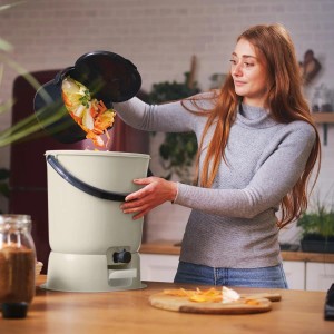 Frau befüllt cremeweißen Skaza Bokashi Komposter mit Bioabfall in Küche.