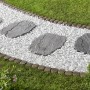 Grau-nuancierte Trittplatten in Natursteinoptik auf einem Gartenweg mit weißen Steinen.