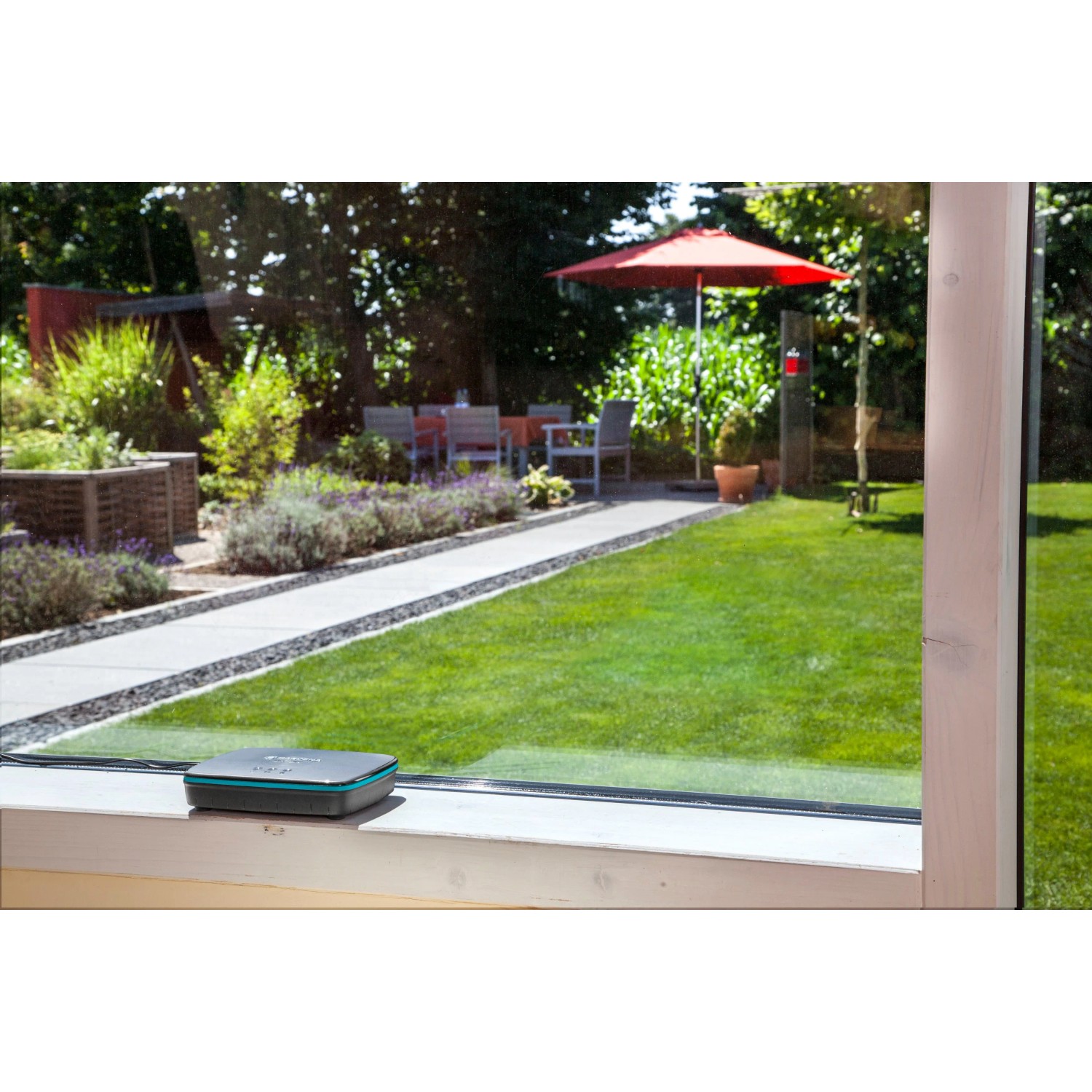 Gardena Smart Water Control Set: Bewässerungscomputer mit Gateway auf Fensterbank, Garten im Hintergrund.
