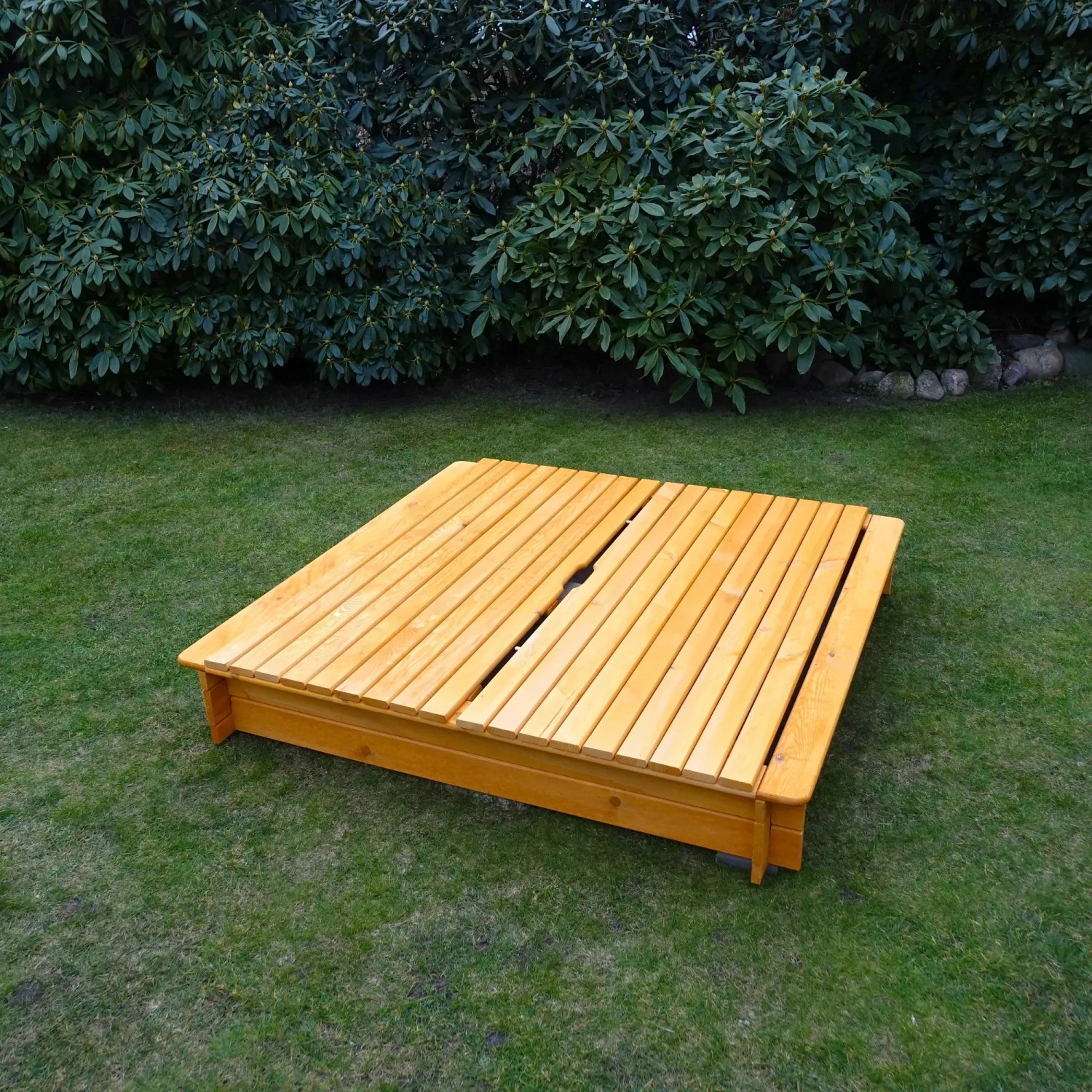 Quadratischer Sandkasten Tessa 140x140 cm aus Holz mit klappbarem Deckel im Garten.