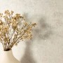 Moderne Vliestapete in Creme Betonoptik mit feiner Struktur, dekoriert mit einer Vase und Trockenblumen.