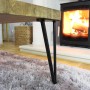 Schwarzes Hairpin Tischbein (2 Streben) an Holztisch auf flauschigem Teppich, Kamin im Hintergrund.