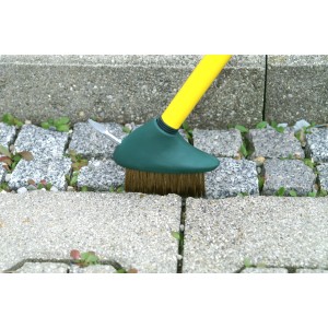Florasun Unkrautfugenbürste mit gelbem Stiel und Kupferborsten im Einsatz auf Pflastersteinen.