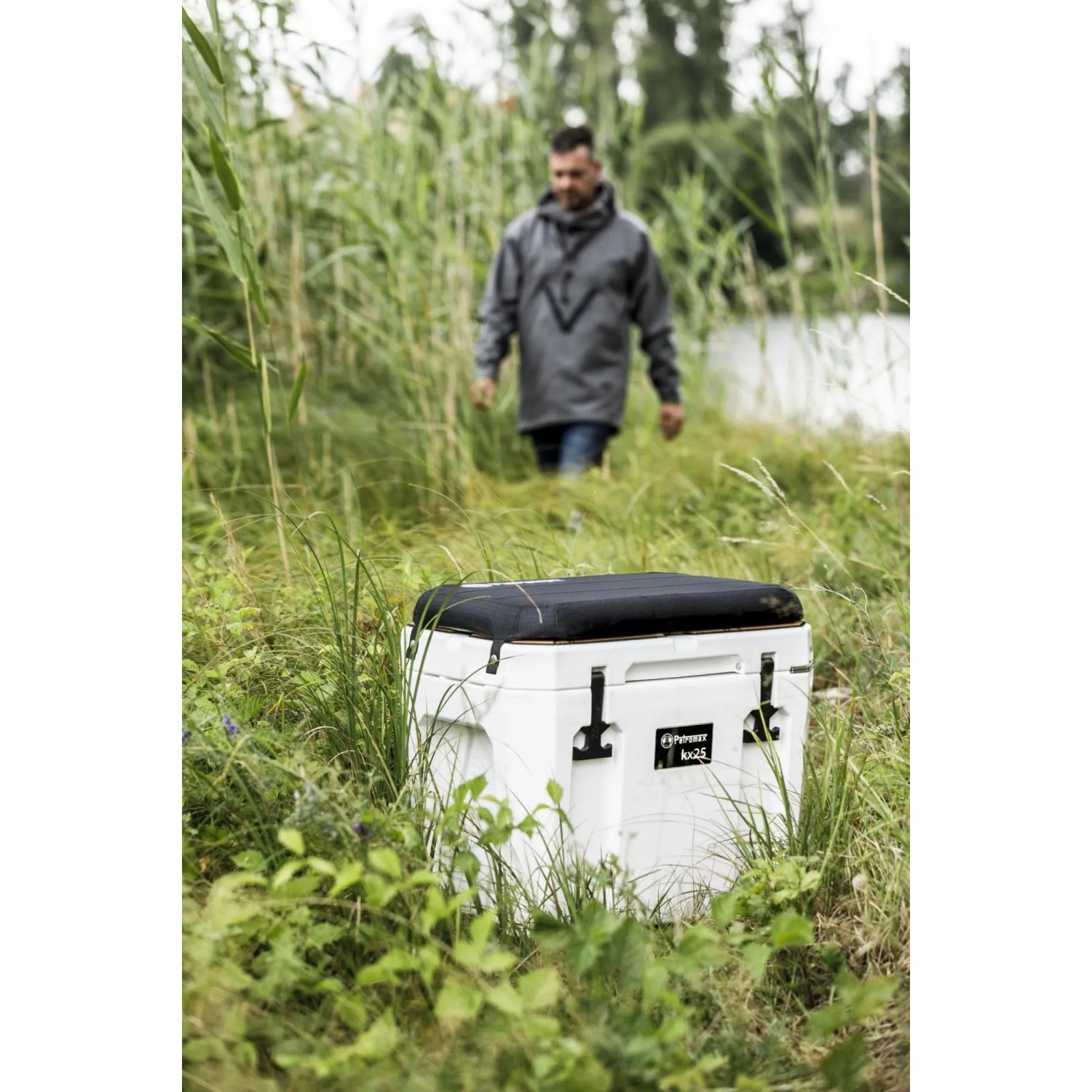 Petromax Kühlbox kx25 mit schwarzem Sitzkissen im Outdoor-Einsatz. Bequeme Sitzgelegenheit für unterwegs.