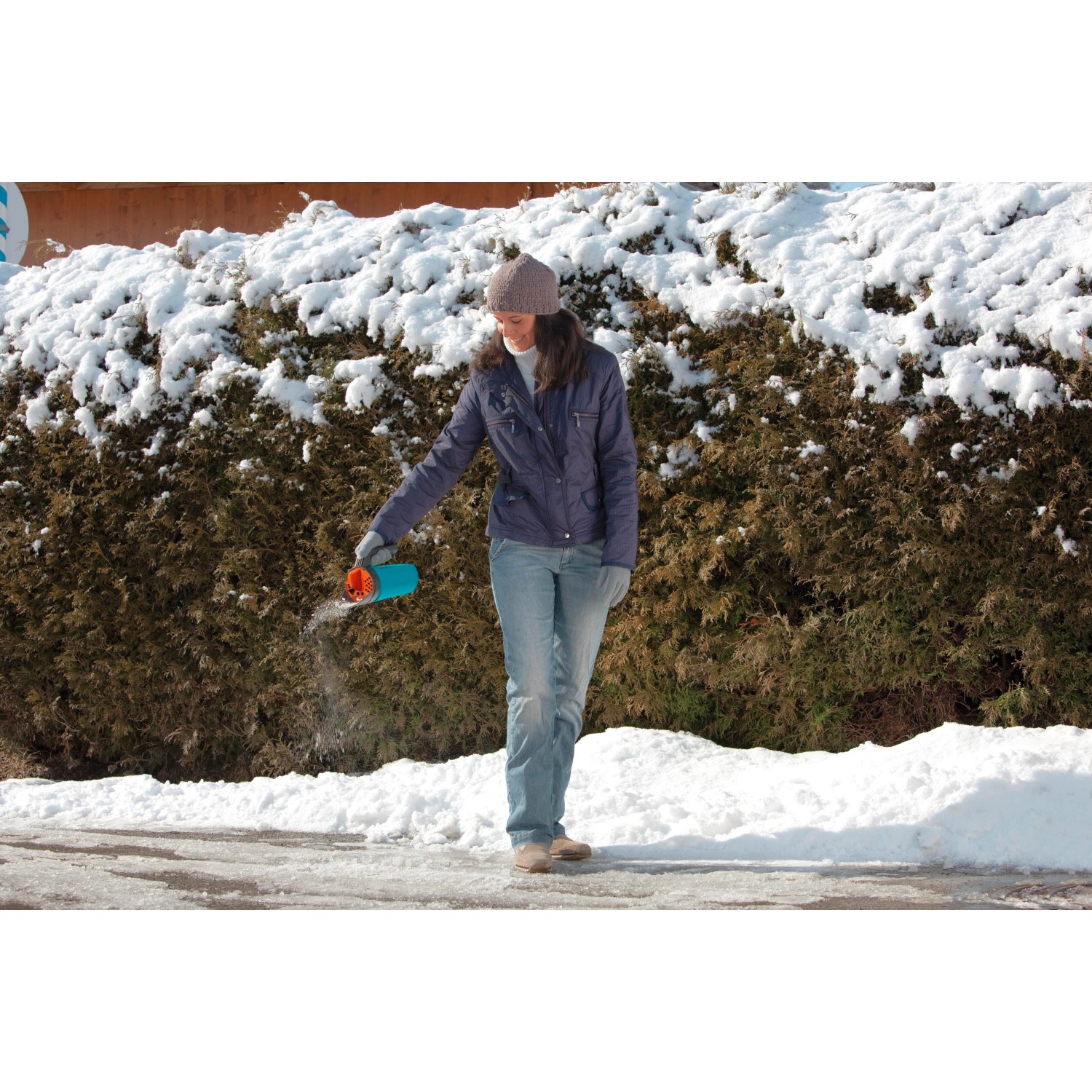 Frau streut mit türkisem Gardena Kleinstreuer S Winterstreugut auf vereister Fläche.