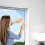 Frau befestigt weißes Windhager Fliegengitter Plus am Fenster. Insektenschutz für Zuhause.