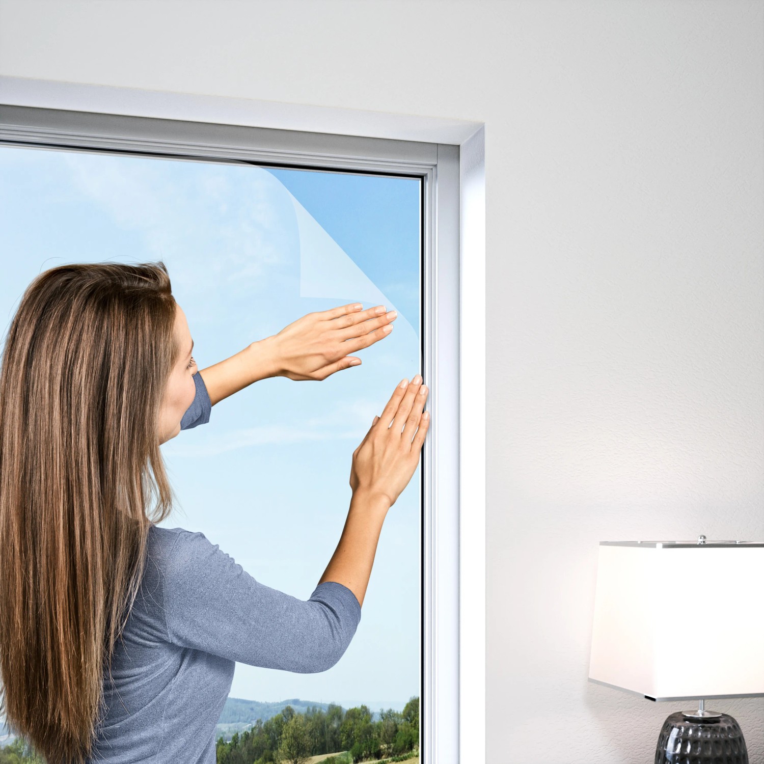 Frau befestigt weißes Windhager Fliegengitter Plus am Fenster. Insektenschutz für Zuhause.
