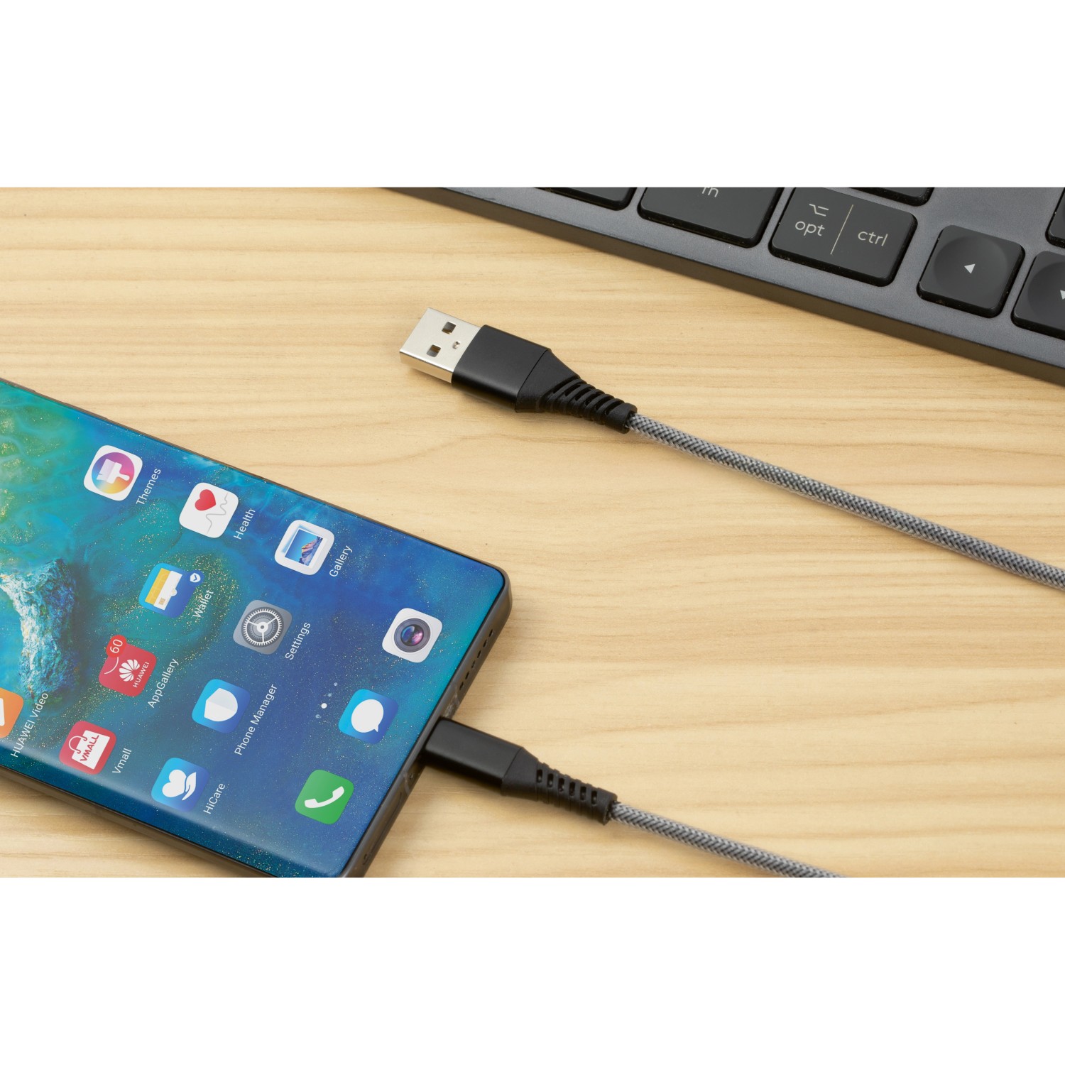 Schwarzes USB-Ladekabel (USB-A auf USB-C) mit Smartphone und Tastatur im Hintergrund.