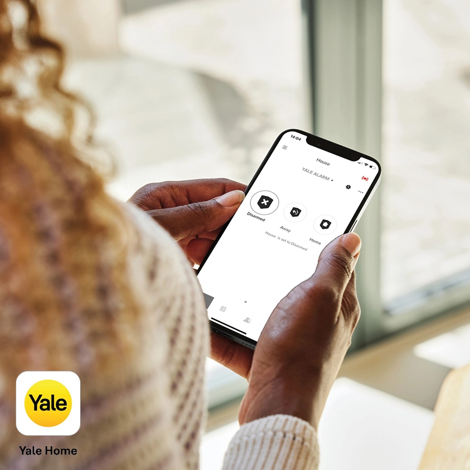 Frau bedient Yale Alarmanlage Smart Alarm Starterkit per App auf Smartphone.