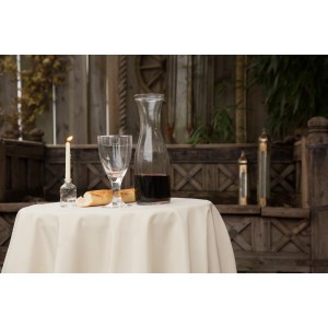 Elegante, runde, elfenbeinfarbene Floracord Tischdecke (160 cm) auf einem Tisch mit Gedeck im Außenbereich.