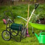 Brauner Relaxdays Gartenschlauchwagen aus Metall mit grünem Schlauch, Kurbel, Rädern und Zubehörkorb im Garten.