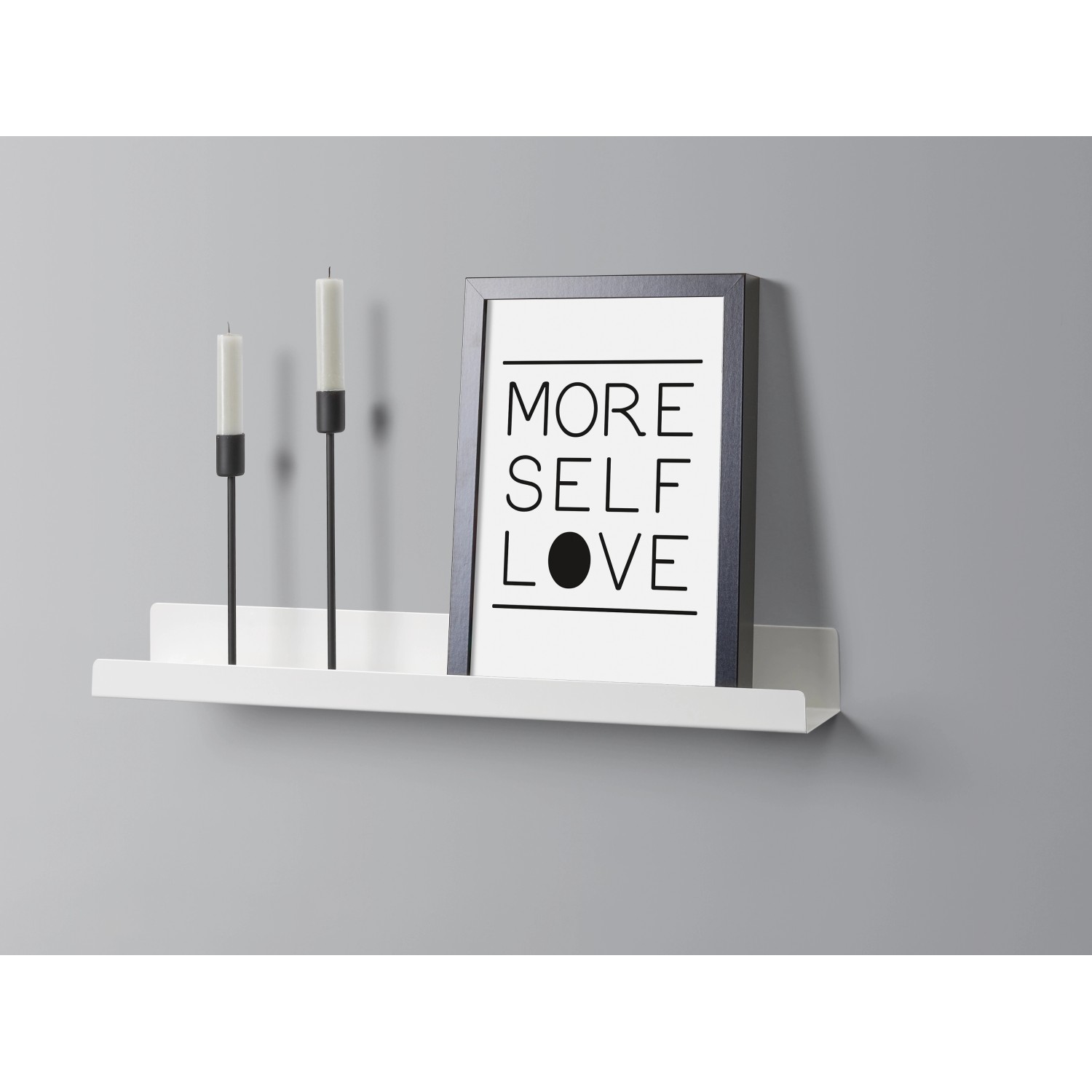 Weißes Metall-Wandregal Bix (60 cm) mit Deko-Elementen wie Kerzen und Bilderrahmen an grauer Wand.