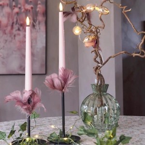 Zwei rosa LED Stabkerzen mit warmweißer 3D Flamme und Timerfunktion in dekorativer Umgebung.