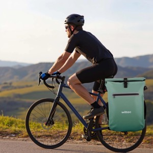 Grüne Wiltec 20L Gepäckträgertasche am Fahrrad eines Radfahrers in bergiger Landschaft. Wasserresistent, als Rucksack nutzbar.