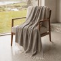 Taupe Sofadecke aus Baumwoll-Mix mit Fransen, auf einem Sessel vor einem Fenster. Ideal für Sofa & Bett.